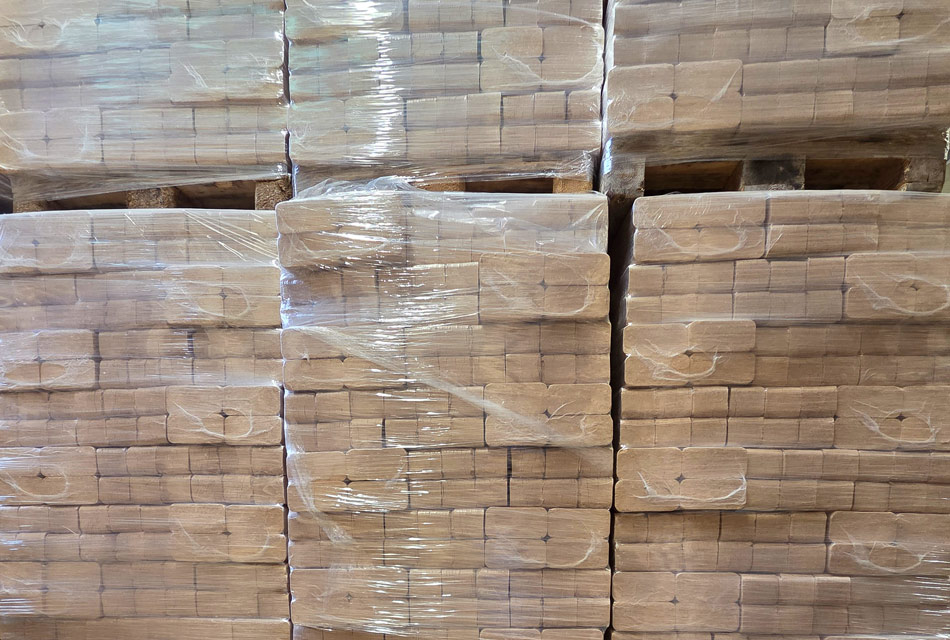Eckige Holzbriketts auf Paletten sind übereinader gestapelt.