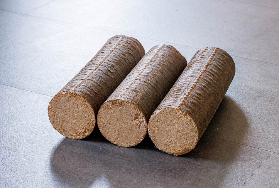 Drei runde Holzbriketts liegen nebeneinder auf Fliesenboden.