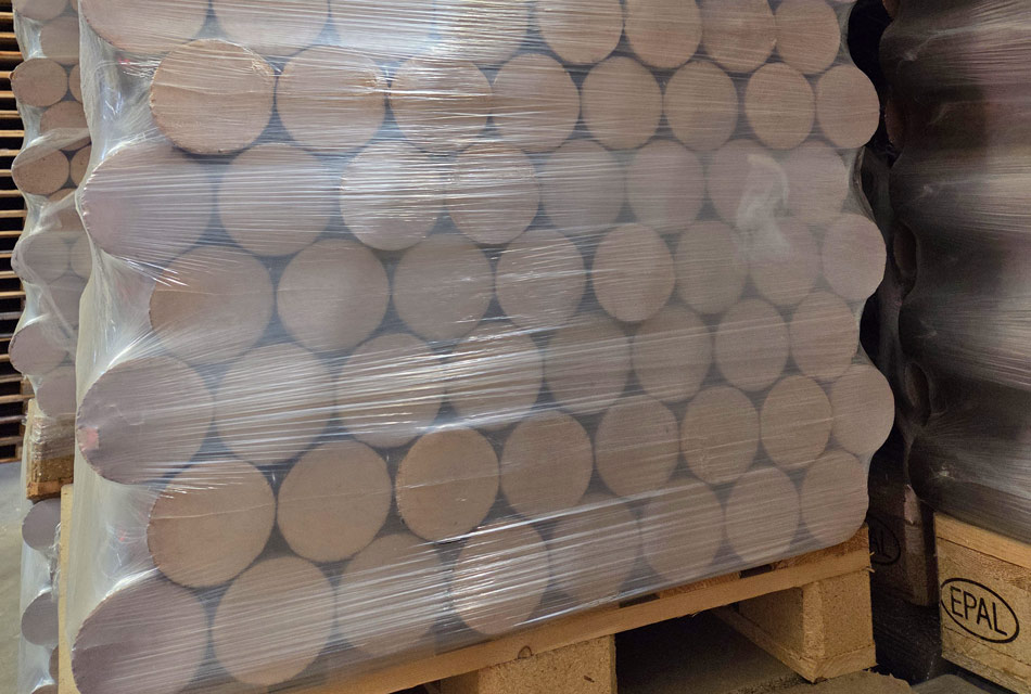 Runde Holzbriketts gestapelt auf einer Palette, sie sind mit Folie umwickelt.